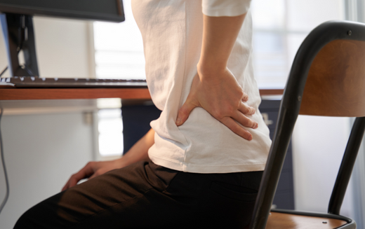 Woman holding her lumbar spine while sitting at office desk